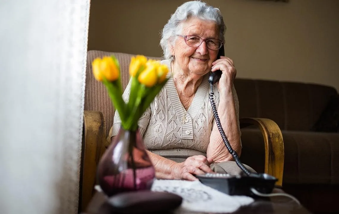An older woman at home smiling while speaking on the telephone